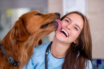 Eine Tierheilpraktikerin mit einem braunen Hund. Der Hund schleckt ihr über die Wange.