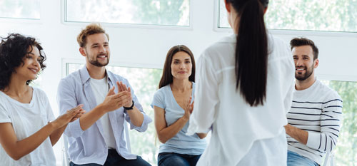 Startseite Heilpraktiker Ausbildung Vier Heilpraktikerschüler sitzen vor einer Frau und machen ihre Handbewegungen nach.